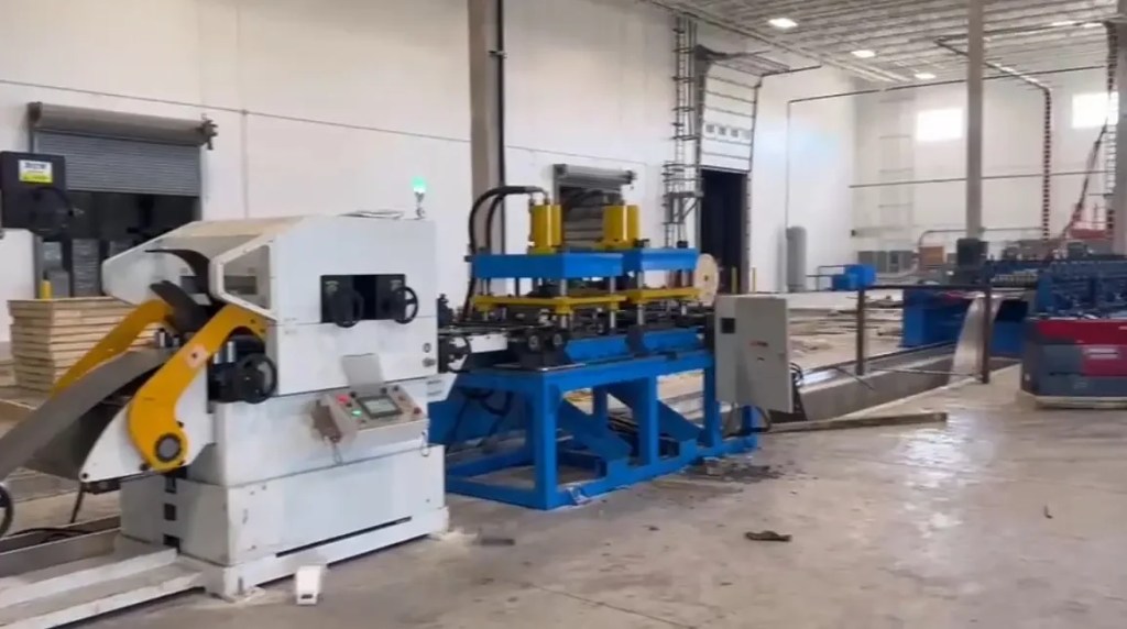 Gros plan sur le servo-alimentateur et le dispositif de poinçonnage hydraulique d'une machine de profilage de pannes Sigma.
