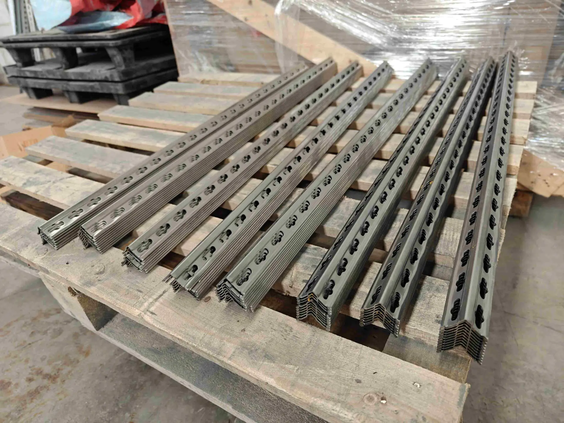 Stapel von präzisionsgeschnittenen, fertig bearbeiteten Metallregalpfosten, die das einheitliche Profil und die durchgehenden Stanzlöcher zeigen.